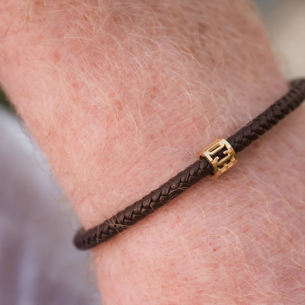 Brown braided bracelet with a gold clasp on a wrist against a blurred background