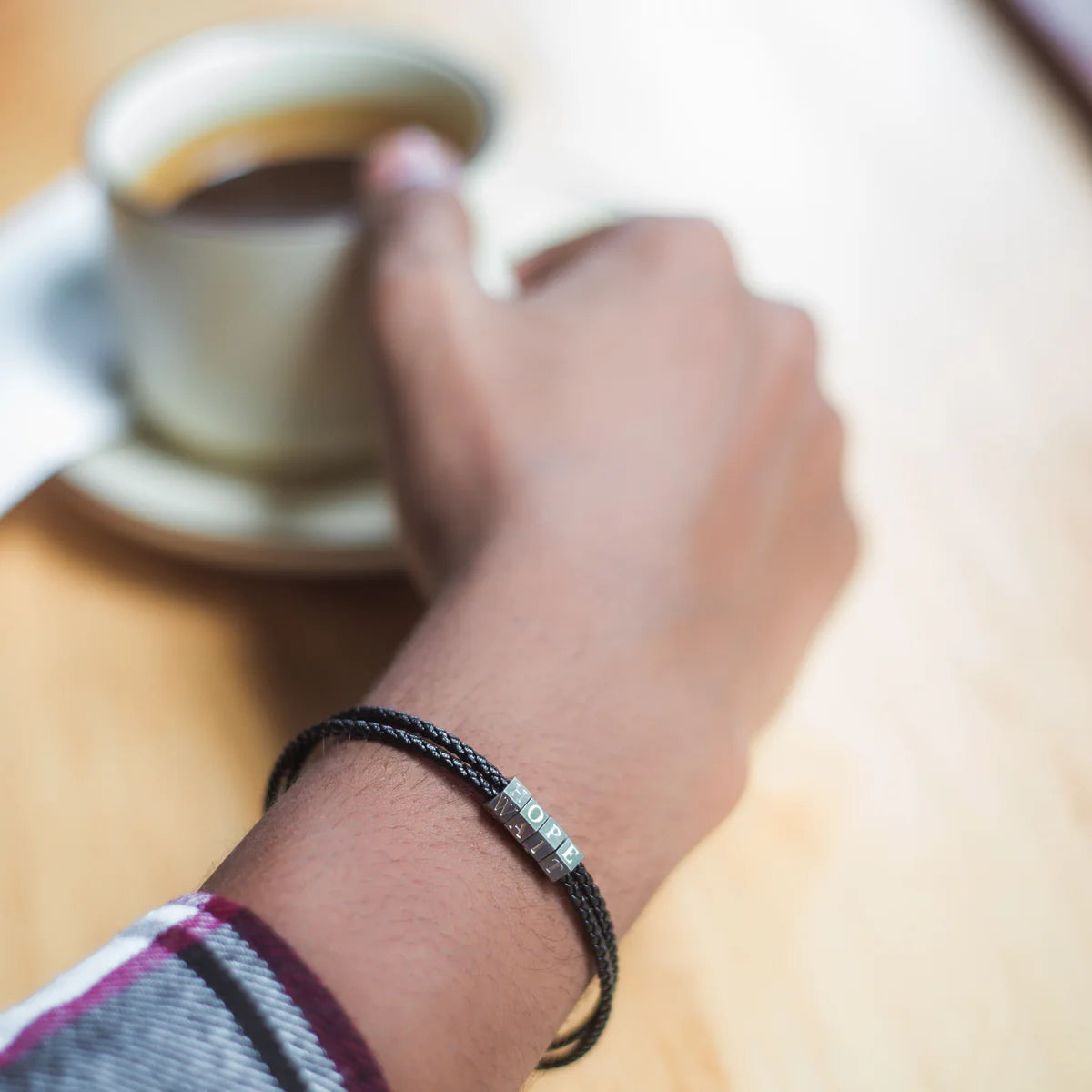 Hand holding a coffee cup with a bracelet featuring small stones.