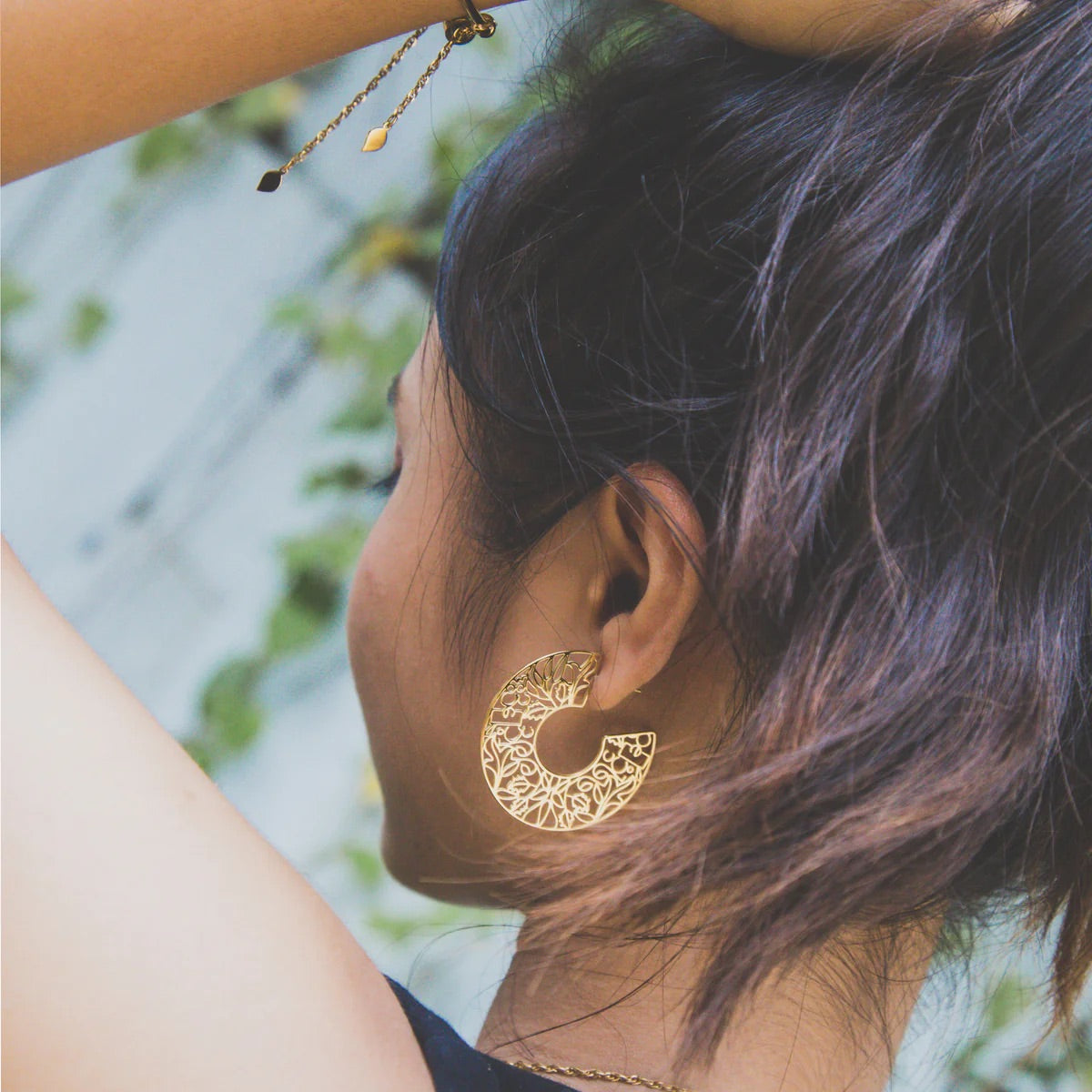Close-up of a person wearing a gold earring with a blurred natural background