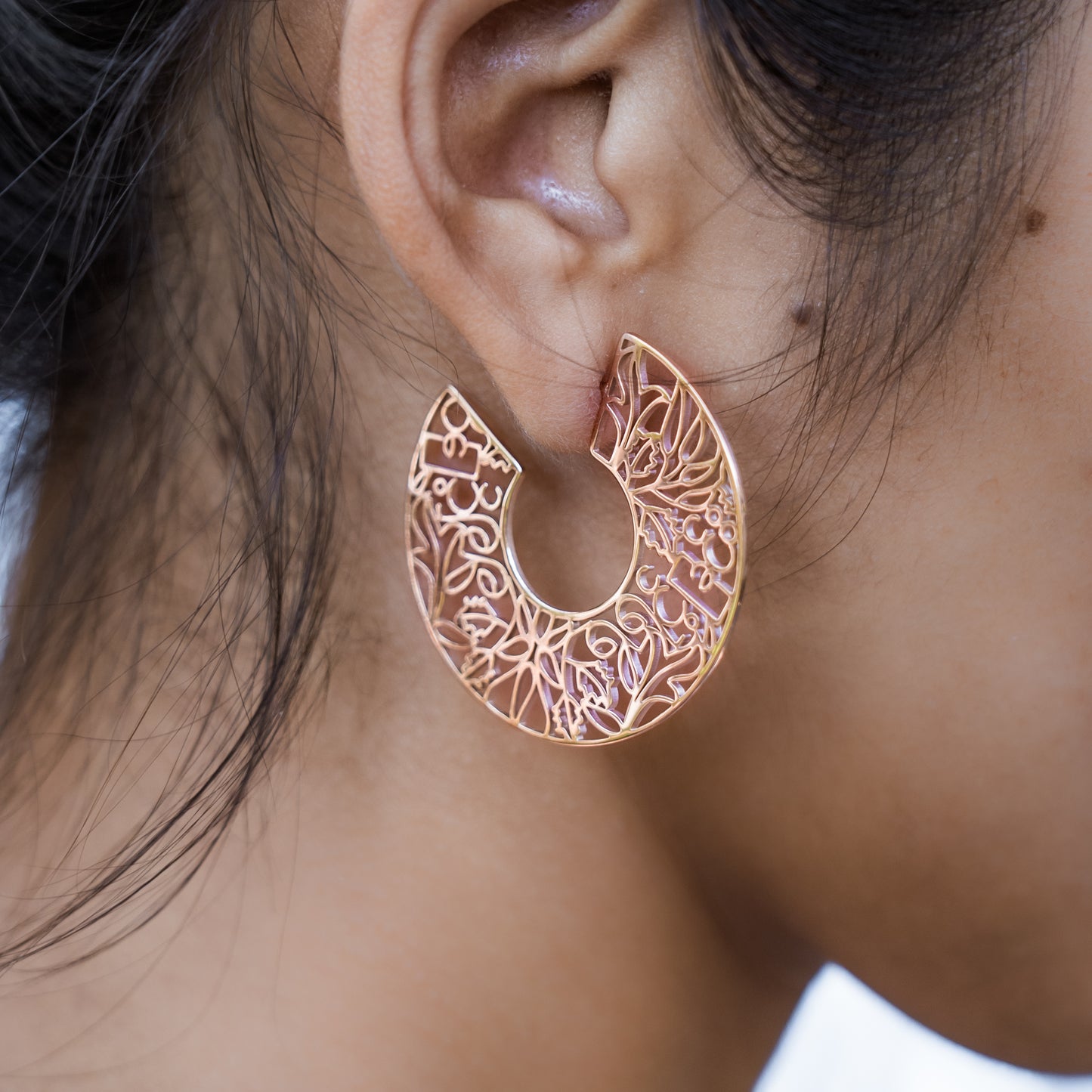 Close-up of a person wearing a rose gold hoop earring with intricate designs.