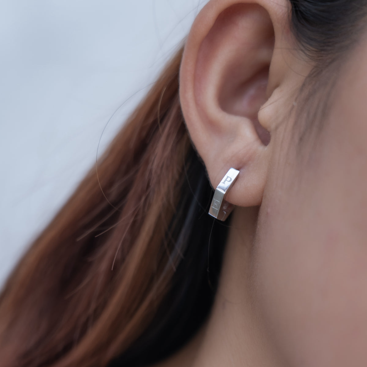Close-up of an ear wearing a silver hoop earring with a blurred background