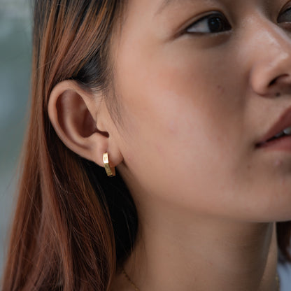 Close-up of a person wearing a gold hoop earring with a blurred background