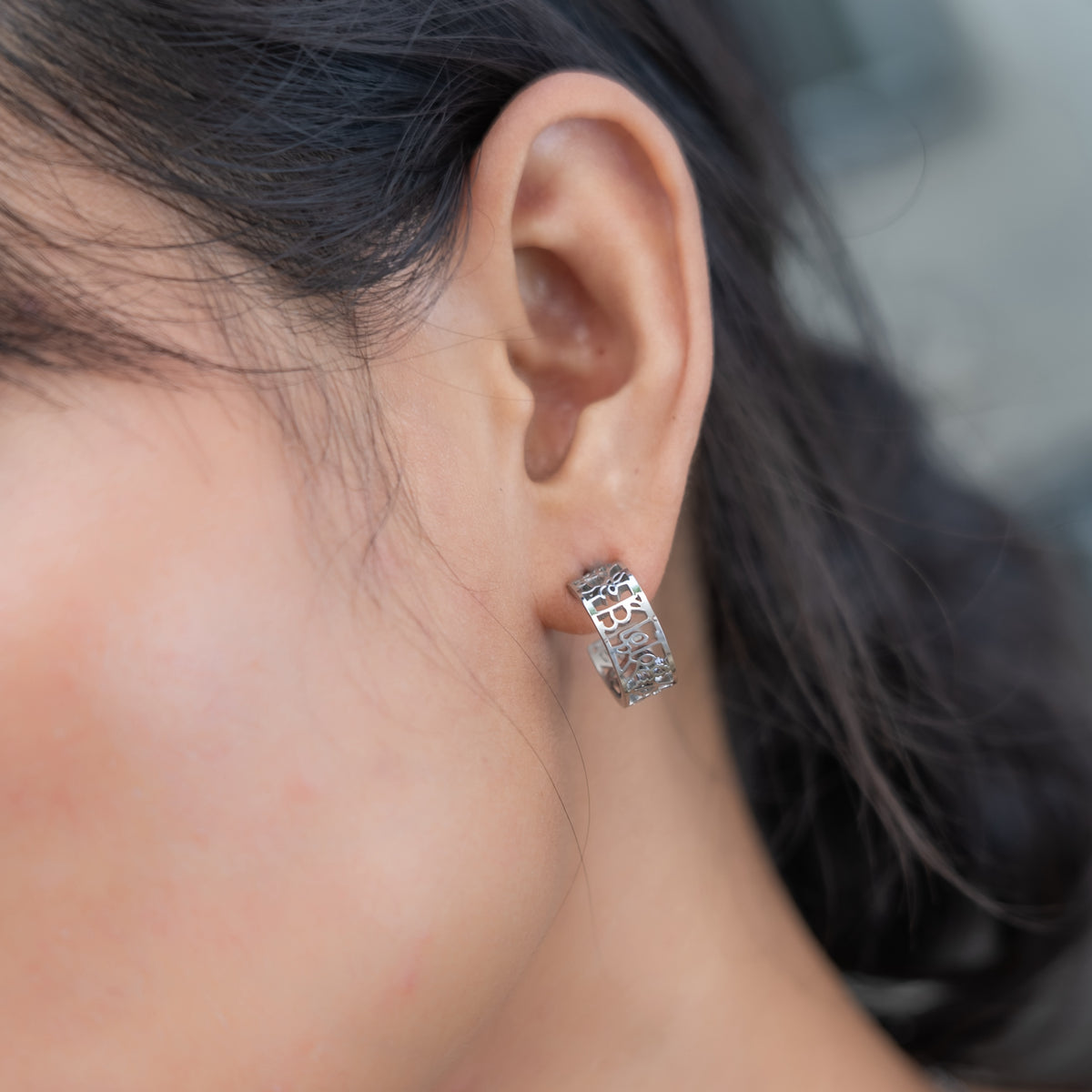 Close-up of an ear wearing a silver hoop earring with a blurred background