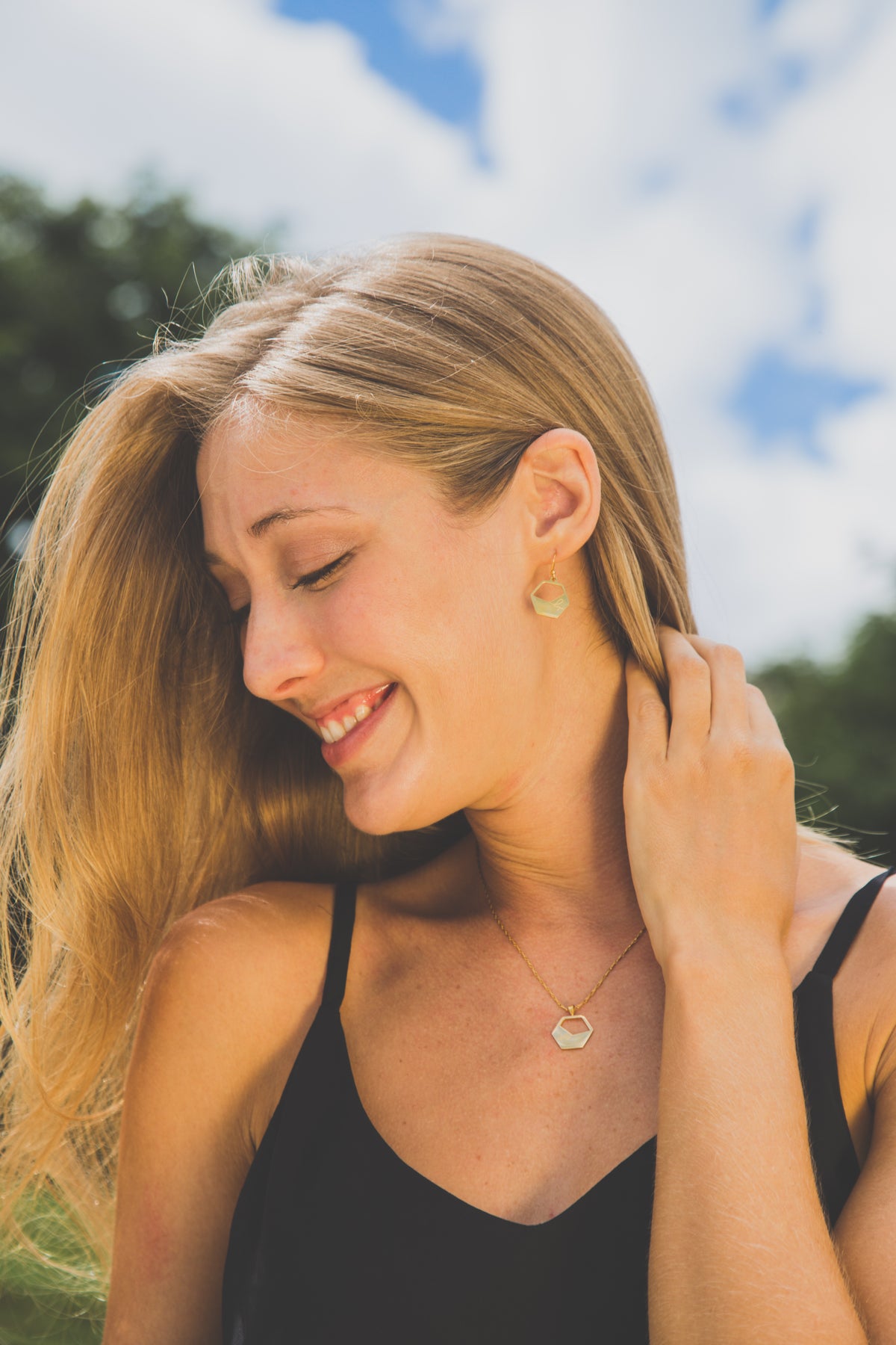 Woman adjusting earring outdoors with blue sky and greenery