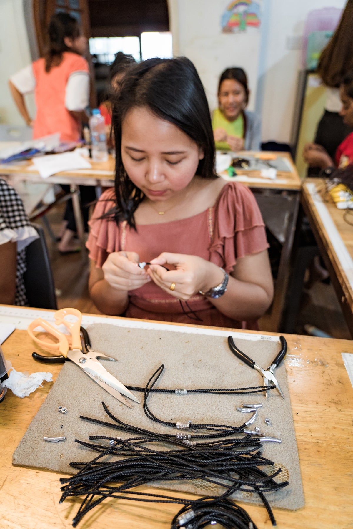 Young girl working on jewelry-making at a table with tools and materials.
