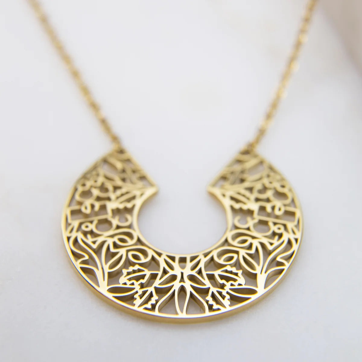 Gold necklace with intricate design on a light background