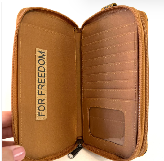 Brown leather wallet with 'For Freedom' label held by a hand on a white background