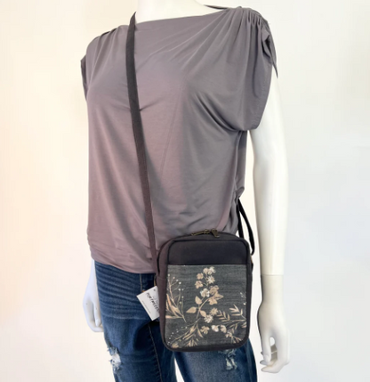 Mannequin wearing a gray top and blue jeans with a black crossbody bag featuring floral design.