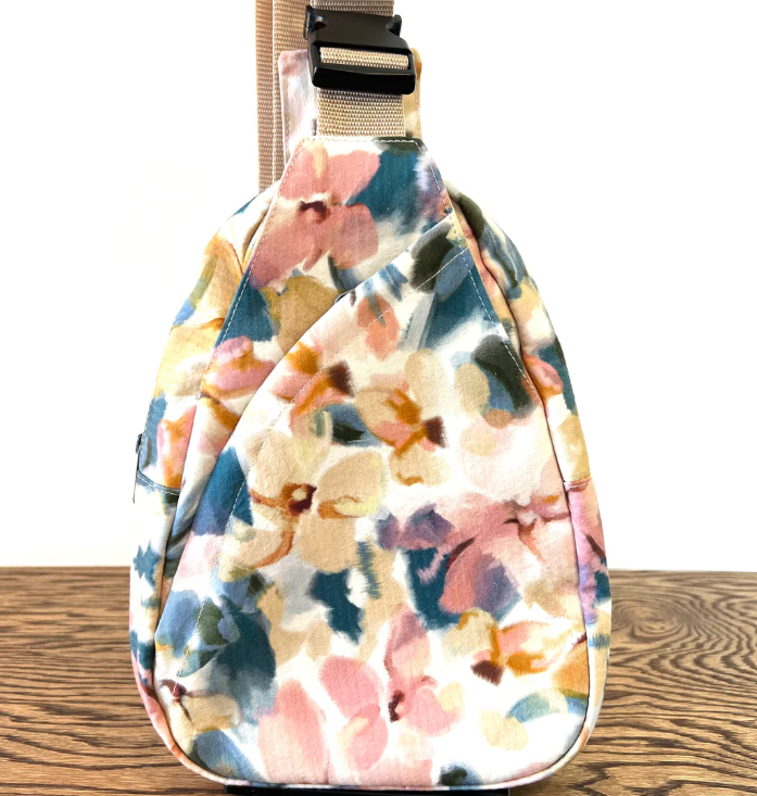 Floral-patterned sling bag on a wooden surface with a white background