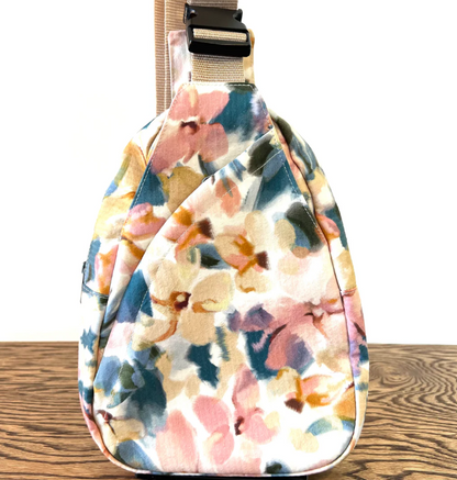 Floral-patterned sling bag on a wooden surface with a white background