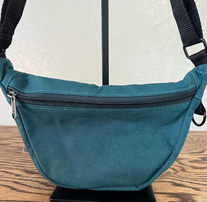 Teal waist bag with a black zipper on a wooden surface