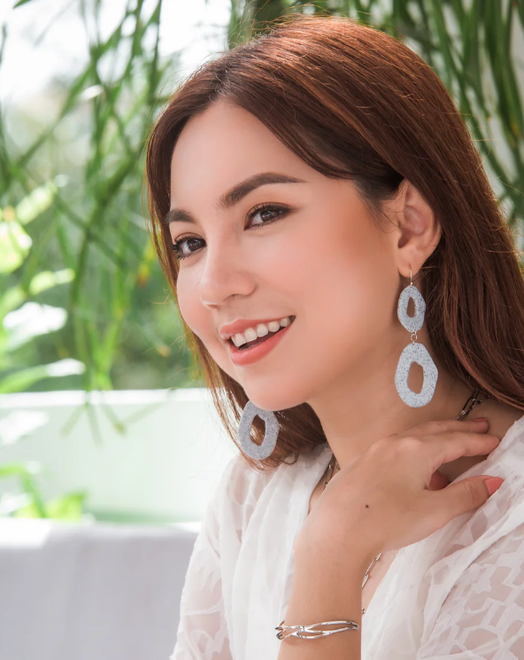 Woman wearing large hoop earrings with a blurred green background