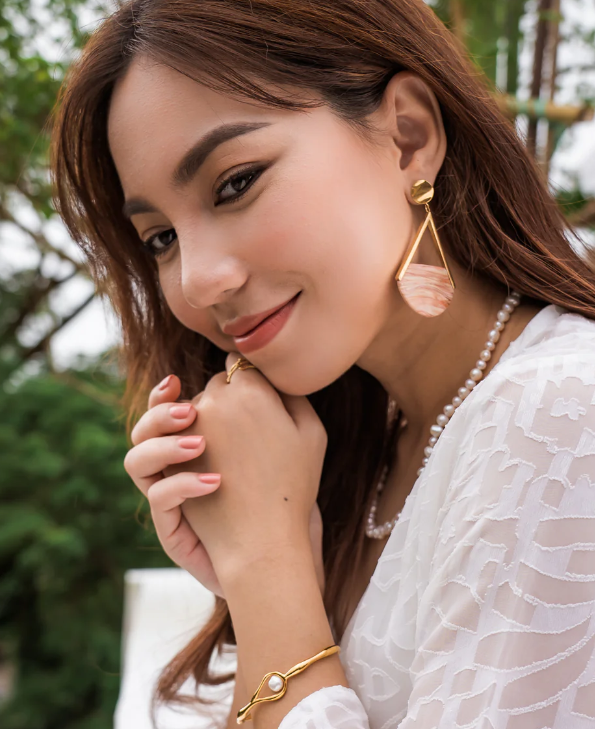 Woman wearing gold earrings and bracelet with a blurred natural background