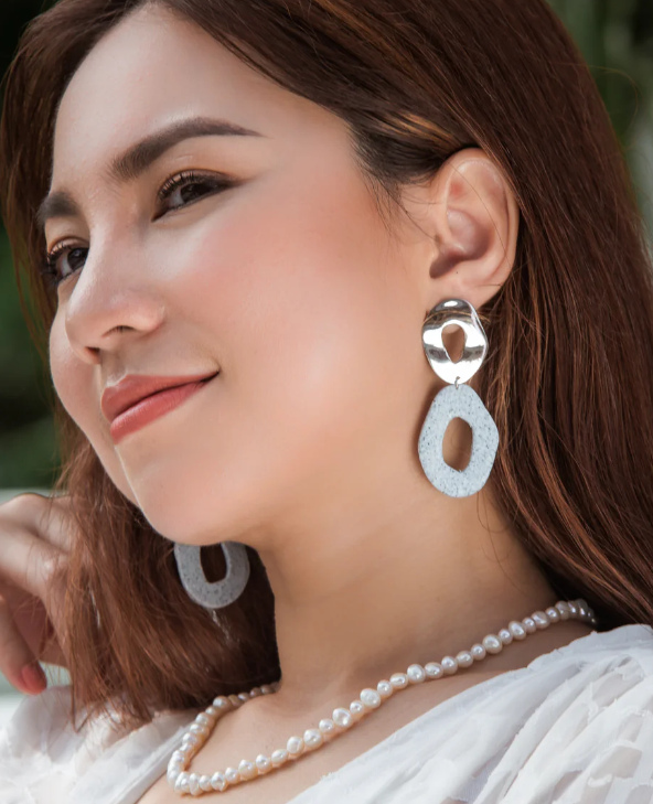 Woman wearing silver earrings and a pearl necklace with a blurred green background