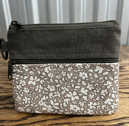 A rectangular zippered pouch with a dark charcoal gray top section and a lower section featuring a white floral pattern on a taupe background, resting on a wooden surface.