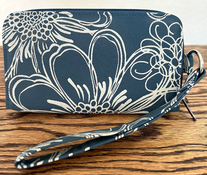 A dark blue fabric clutch wallet with a white floral and scroll pattern, featuring a matching wrist strap and metal ring, displayed on a wooden surface.