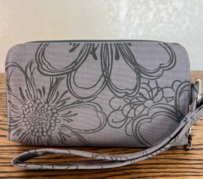 A gray fabric zippered pouch with a black floral line-art pattern and a matching wrist strap, resting on a wooden surface against a light textured wall.