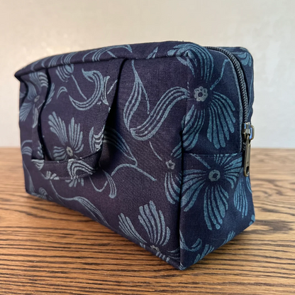 A fabric zippered pouch with a dark navy blue background and a light blue floral pattern, resting on a wooden surface against a light beige wall.