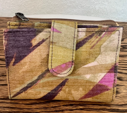 A zippered fabric pouch with a geometric ikat pattern in beige, brown, purple, and pink, resting on a wooden surface.