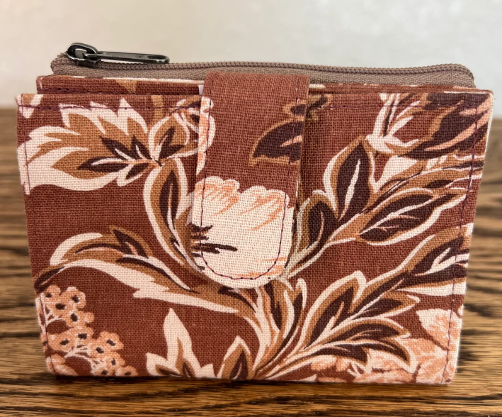 A small zippered pouch or coin purse with a brown, beige, and white floral pattern, resting on a wooden surface.