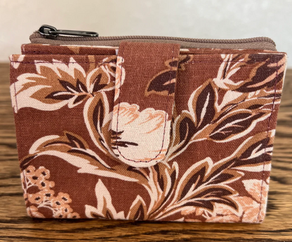 A small zippered pouch or coin purse with a brown, beige, and white floral pattern, resting on a wooden surface.
