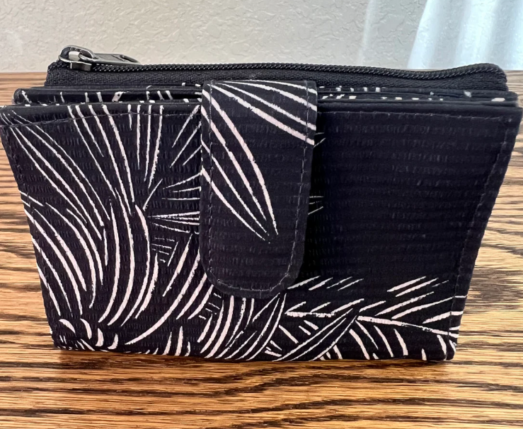 A black and white palm leaf patterned zippered pouch with a front flap, resting on a wooden table.
