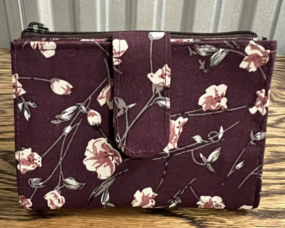 A dark purple fabric zippered pouch with a floral print of pink and white flowers and gray-green stems, resting on a wooden surface.
