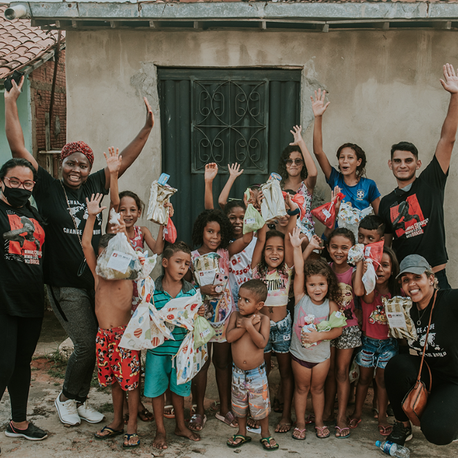 Group of people and children standing together, holding bags, in front of a building.