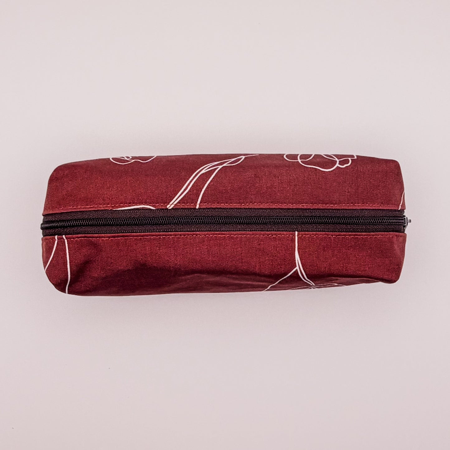 Red pouch with white floral patterns and a black zipper on a light pink background
