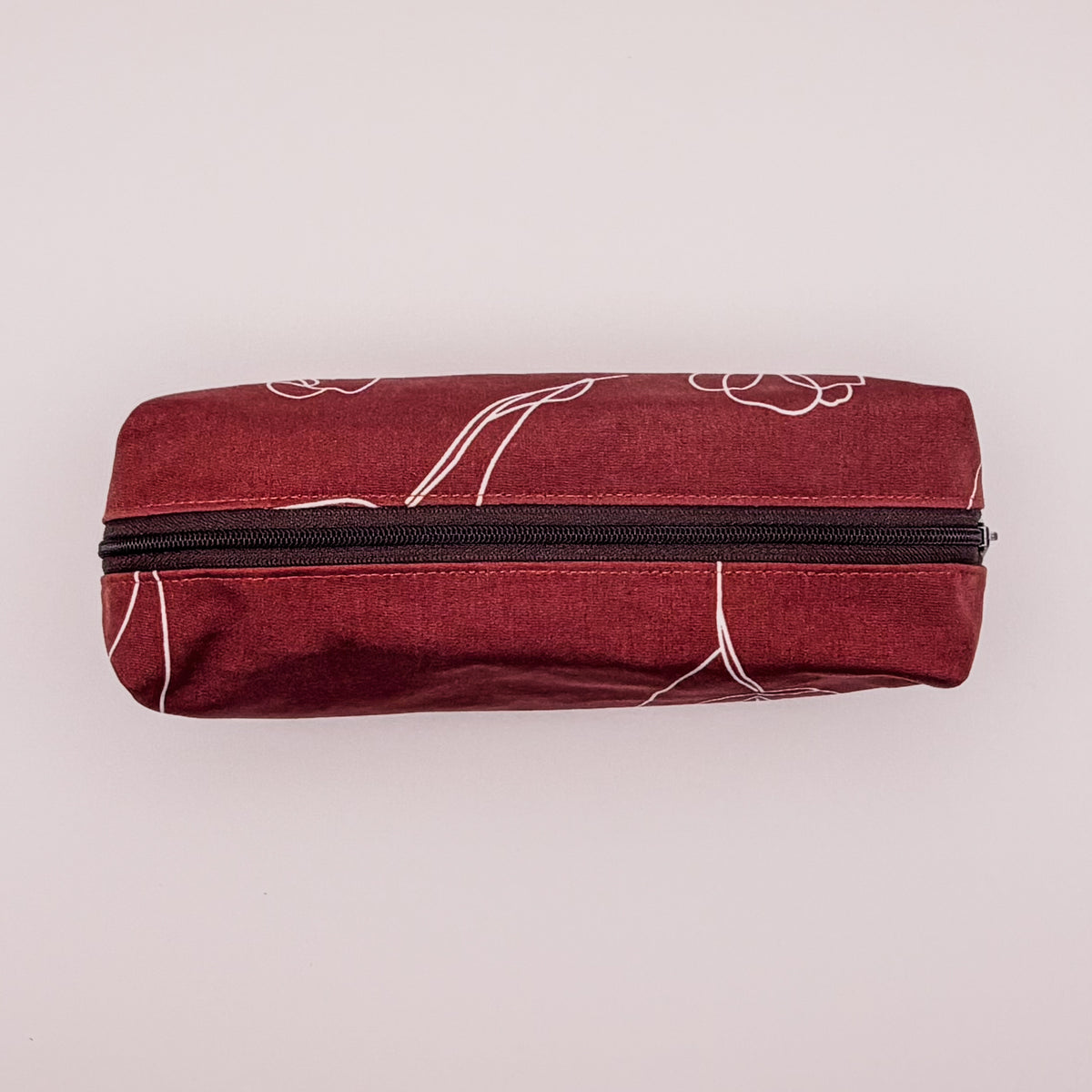 Red pouch with white floral patterns and a black zipper on a light pink background