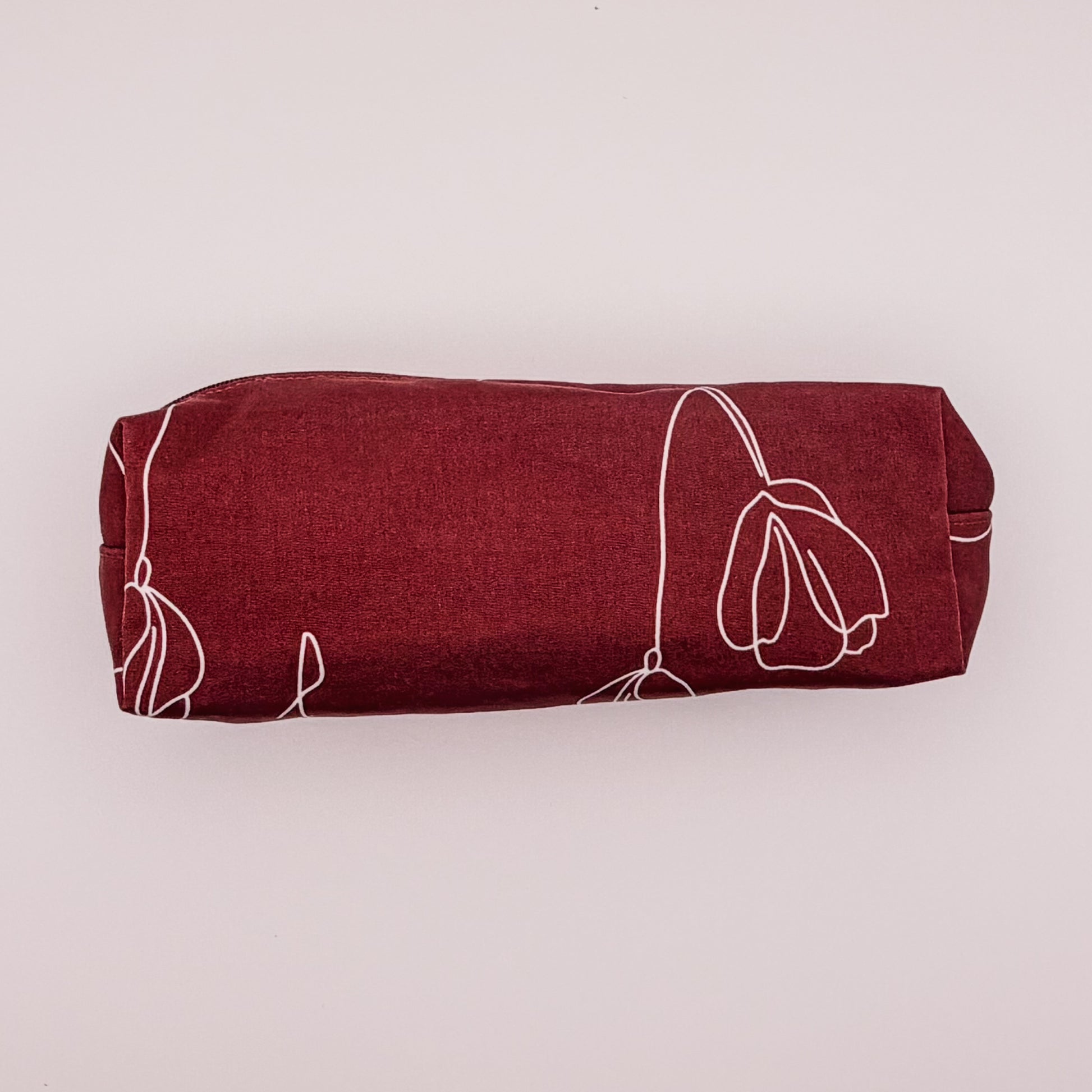 Red pouch with white floral patterns and a black zipper on a light pink background