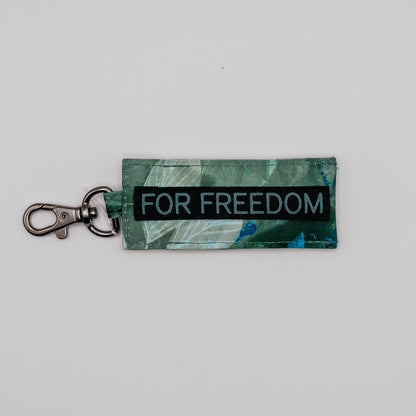 Keychain with 'FOR FREEDOM' text on a green patterned background