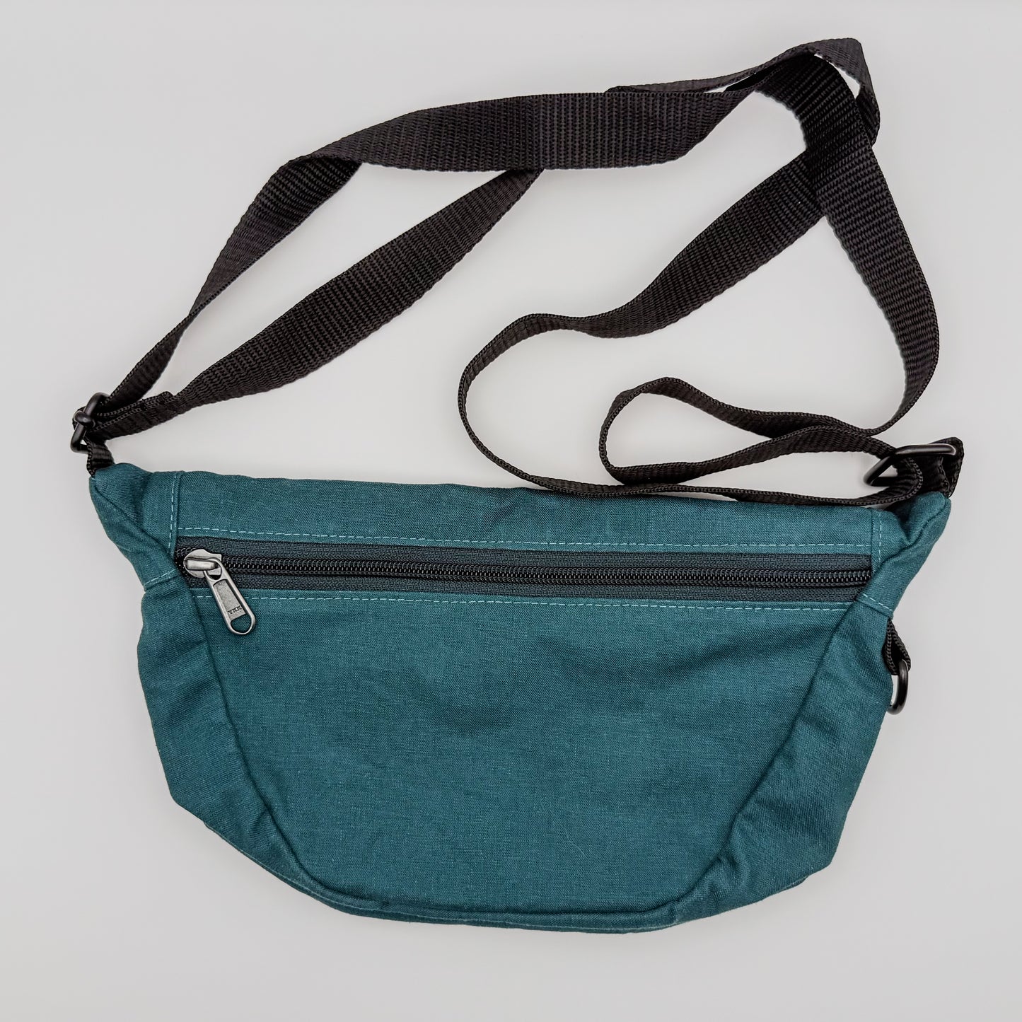 Teal waist bag with a black strap on a light gray background