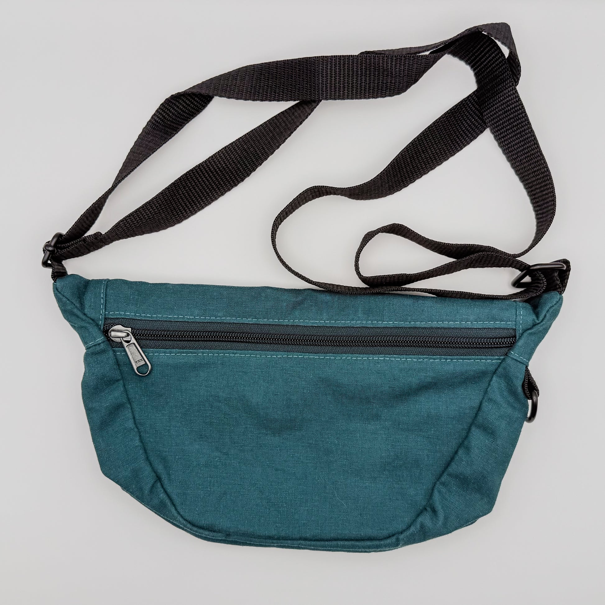 Teal waist bag with a black strap on a light gray background
