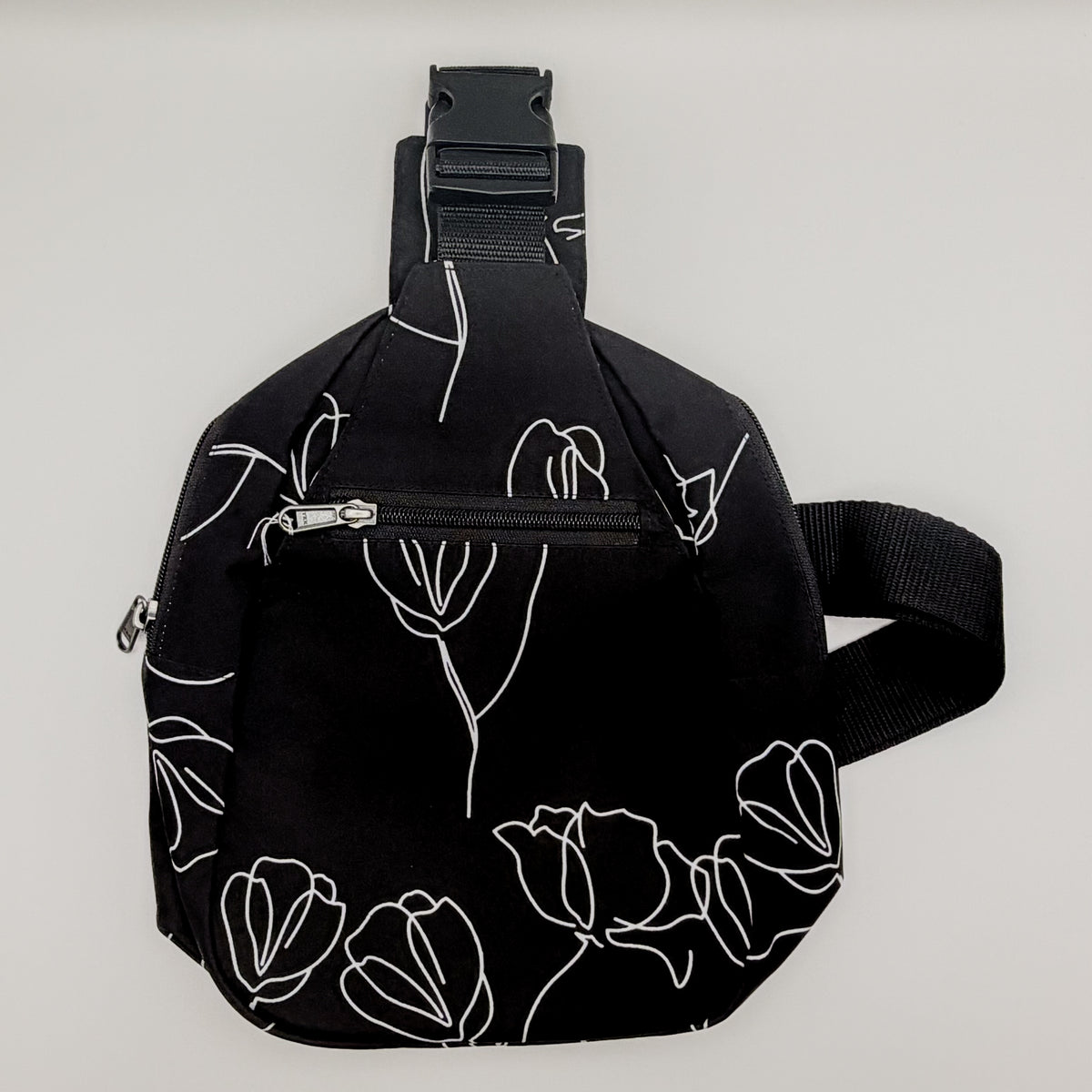 Black sling bag with white floral patterns on a light gray background