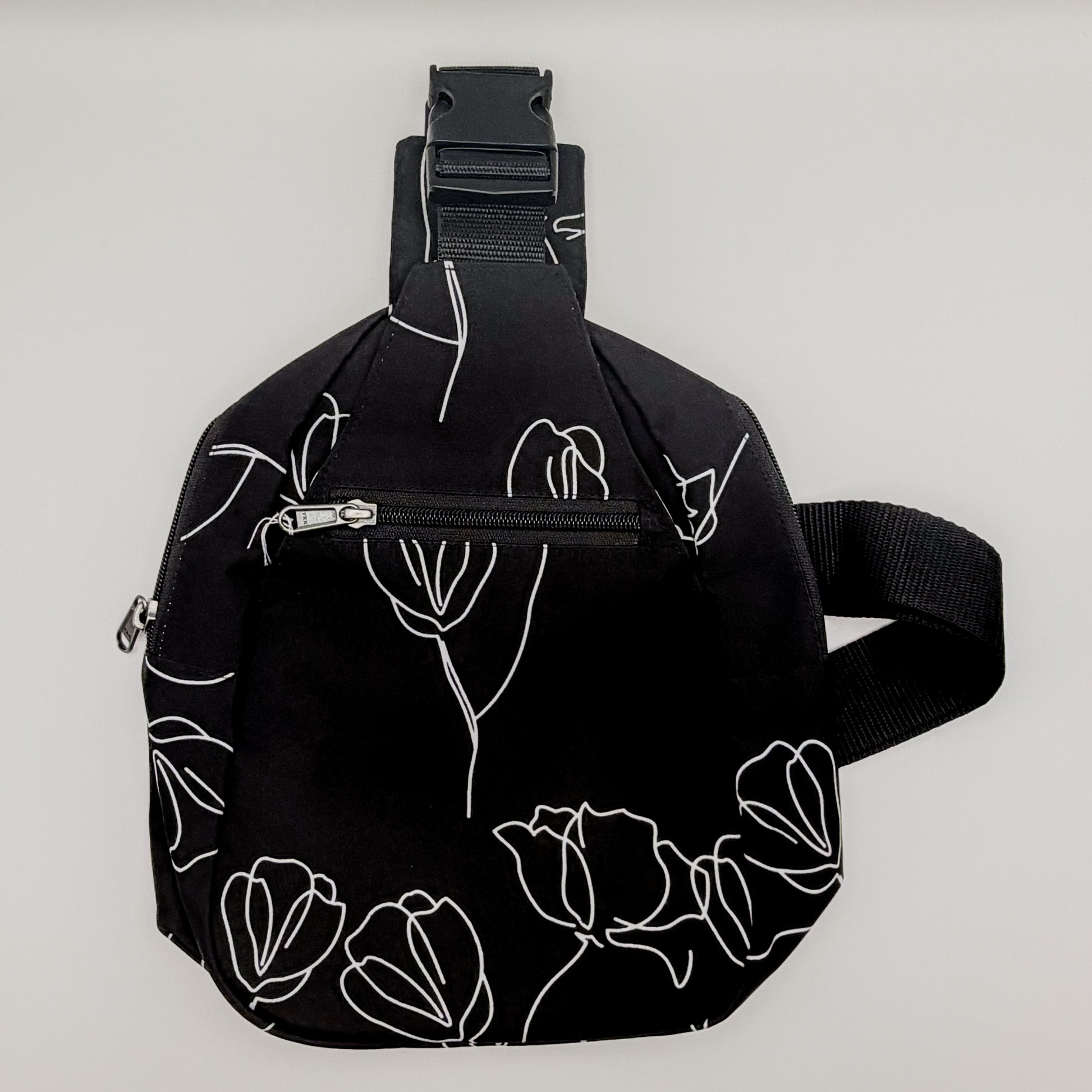 Black sling bag with white floral patterns on a light gray background
